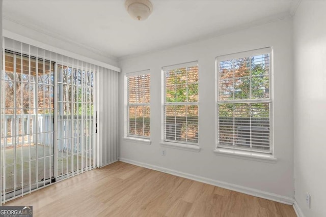 empty room featuring a wealth of natural light, ornamental molding, and wood-type flooring