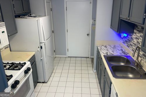 kitchen featuring light tile patterned floors, gray cabinets, backsplash, white gas stove, and sink