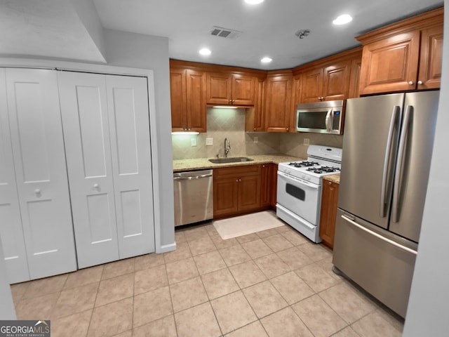 kitchen with appliances with stainless steel finishes, decorative backsplash, sink, light stone counters, and light tile patterned floors