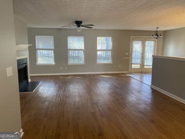 unfurnished living room featuring built in features, dark hardwood / wood-style flooring, ceiling fan with notable chandelier, and a textured ceiling