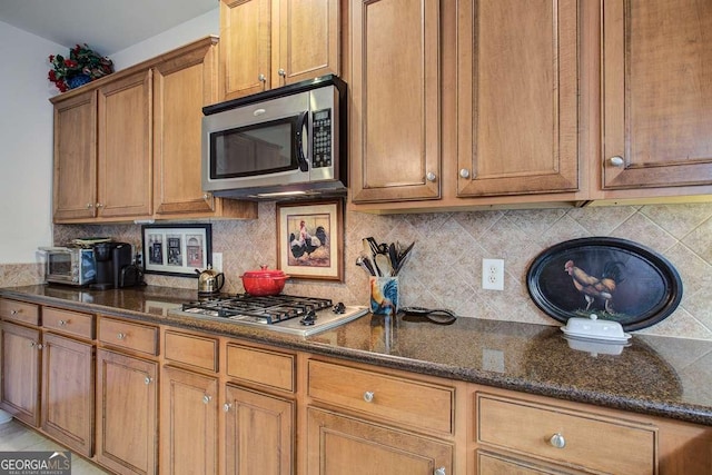 kitchen with appliances with stainless steel finishes, dark stone counters, and tasteful backsplash