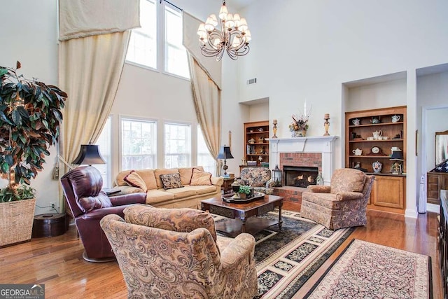 living room with built in shelves, wood-type flooring, a brick fireplace, and a chandelier