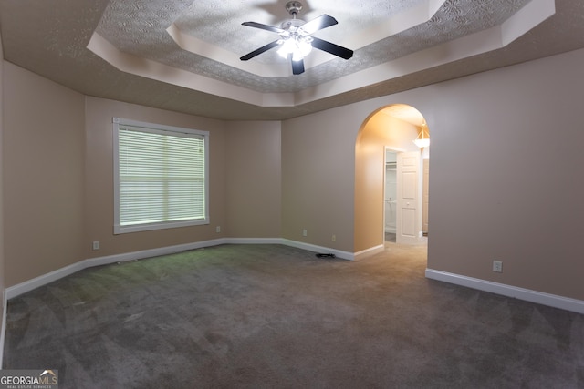 carpeted empty room with a textured ceiling, ceiling fan, and a tray ceiling