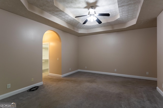 unfurnished room featuring a raised ceiling, ceiling fan, a textured ceiling, and dark colored carpet