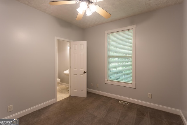 unfurnished bedroom with ceiling fan, ensuite bath, dark carpet, and a textured ceiling