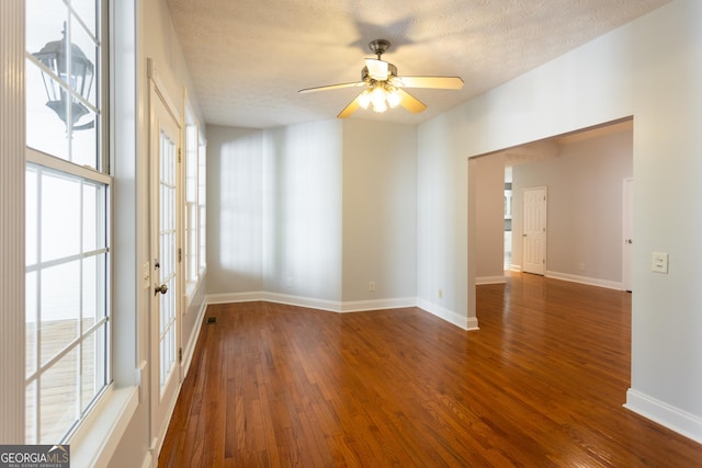 empty room with ceiling fan, dark hardwood / wood-style flooring, a wealth of natural light, and a textured ceiling