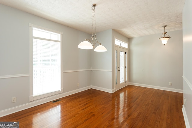 empty room featuring a notable chandelier, a textured ceiling, and hardwood / wood-style floors