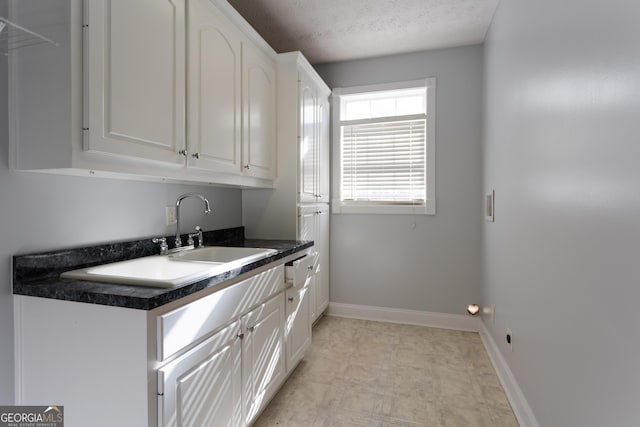 kitchen with a textured ceiling, white cabinetry, and sink