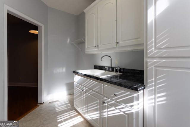 kitchen featuring white cabinets, dark stone counters, and sink