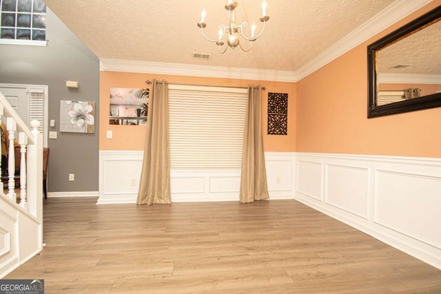 unfurnished dining area featuring light hardwood / wood-style floors, a textured ceiling, crown molding, and an inviting chandelier