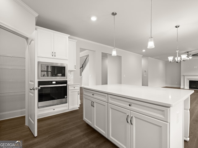 kitchen featuring decorative light fixtures, oven, a kitchen island, built in microwave, and white cabinets