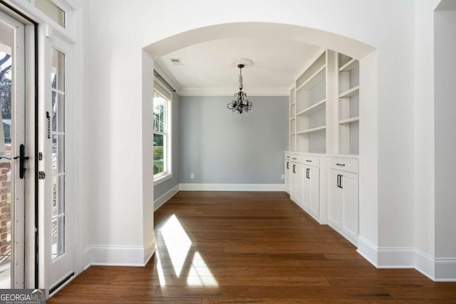 unfurnished dining area with built in shelves, dark wood-type flooring, and a notable chandelier