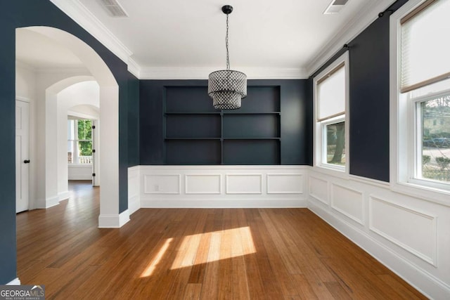 unfurnished dining area with wood-type flooring, built in shelves, and ornamental molding