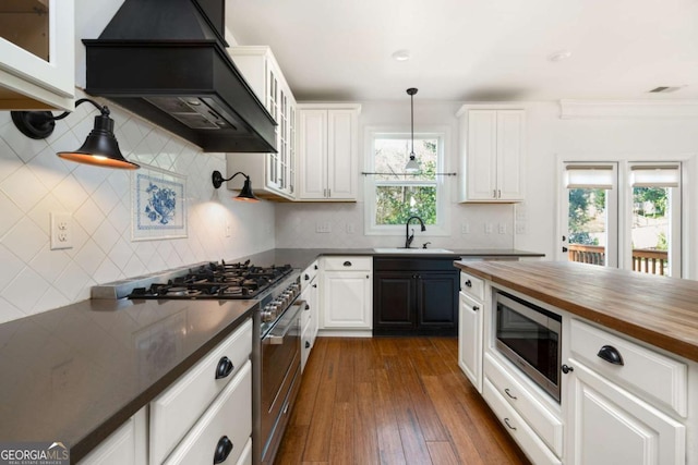 kitchen with white cabinets, appliances with stainless steel finishes, wooden counters, sink, and custom range hood