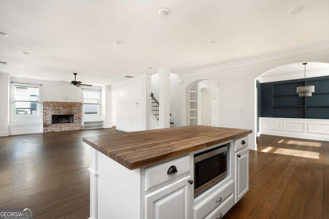 kitchen featuring a brick fireplace, a kitchen island, white cabinets, butcher block counters, and ceiling fan with notable chandelier