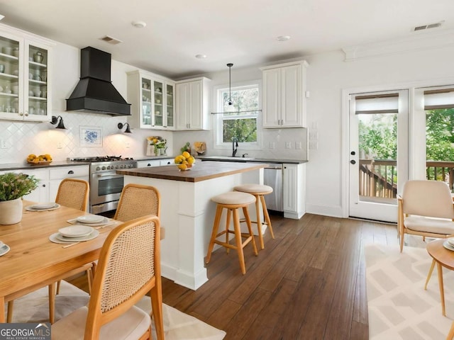 kitchen featuring premium range hood, white cabinetry, hanging light fixtures, appliances with stainless steel finishes, and dark hardwood / wood-style flooring