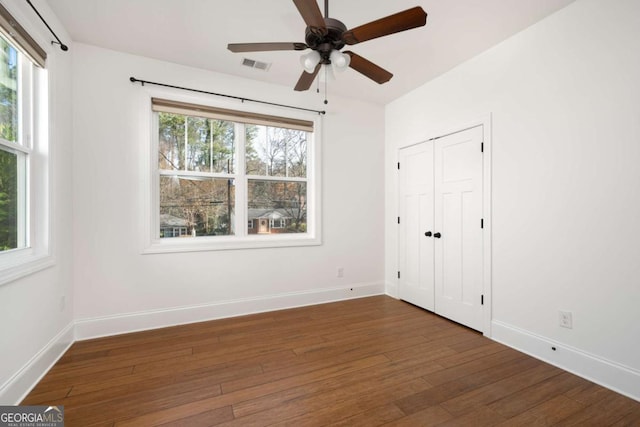 unfurnished bedroom with ceiling fan, a closet, dark hardwood / wood-style floors, and multiple windows