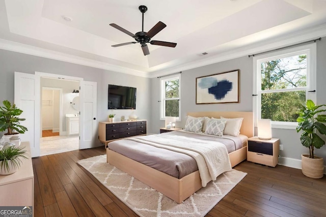 bedroom with ceiling fan, dark hardwood / wood-style flooring, a raised ceiling, and ensuite bath