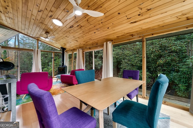 sunroom featuring vaulted ceiling, ceiling fan, wood ceiling, and a wood stove