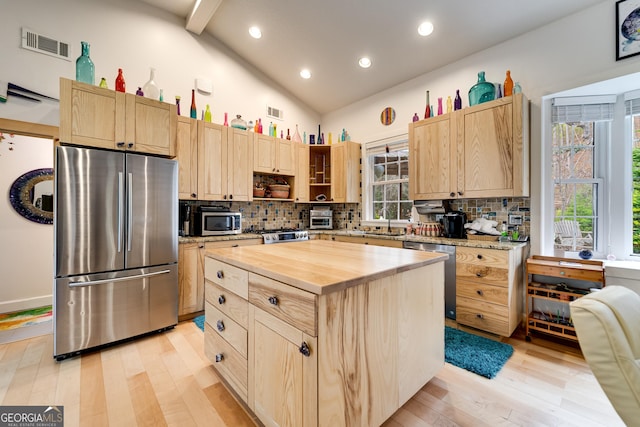 kitchen featuring a center island, lofted ceiling with beams, appliances with stainless steel finishes, light brown cabinets, and butcher block counters