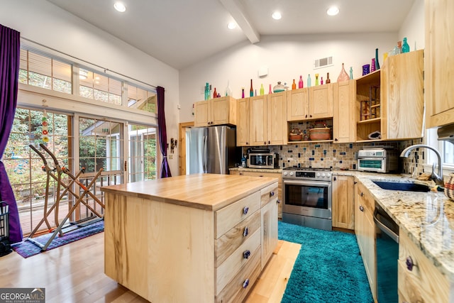 kitchen with beam ceiling, light brown cabinetry, stainless steel appliances, and a kitchen island