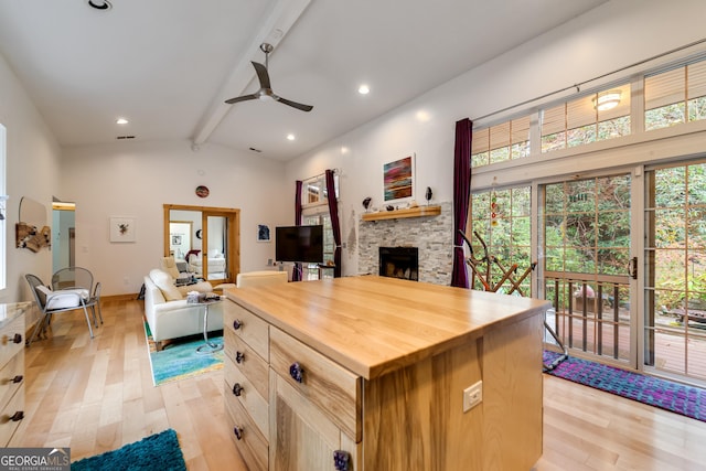 kitchen with a center island, a stone fireplace, beamed ceiling, ceiling fan, and butcher block countertops