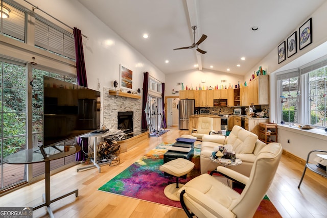 living room featuring ceiling fan, vaulted ceiling with beams, a stone fireplace, and light hardwood / wood-style floors