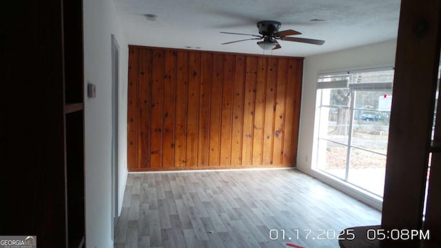 empty room featuring ceiling fan, light hardwood / wood-style floors, and wooden walls