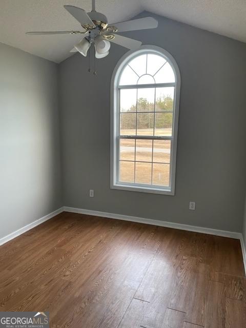 spare room with ceiling fan, dark wood-type flooring, a textured ceiling, and lofted ceiling