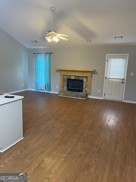 unfurnished living room featuring ceiling fan, hardwood / wood-style floors, and a stone fireplace