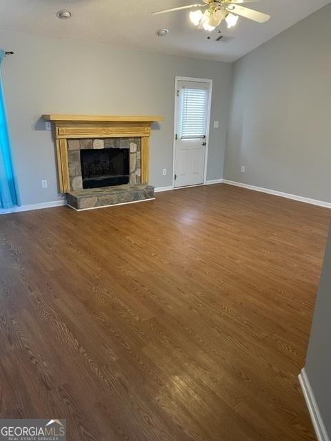 unfurnished living room with ceiling fan, dark hardwood / wood-style flooring, and a stone fireplace