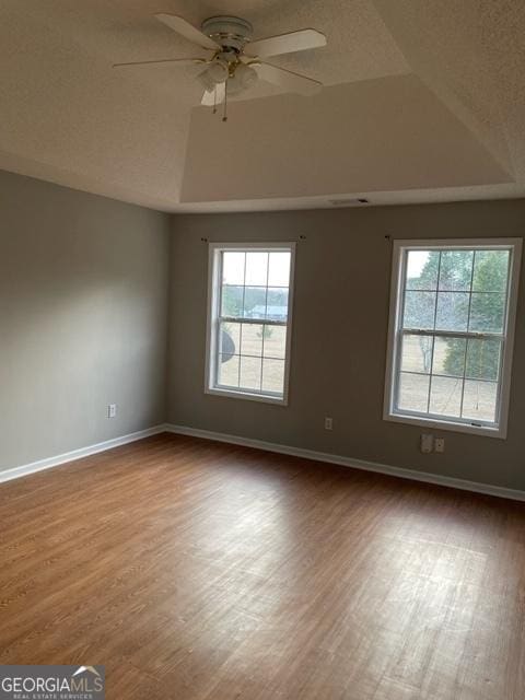 empty room with ceiling fan, a tray ceiling, a textured ceiling, and hardwood / wood-style floors