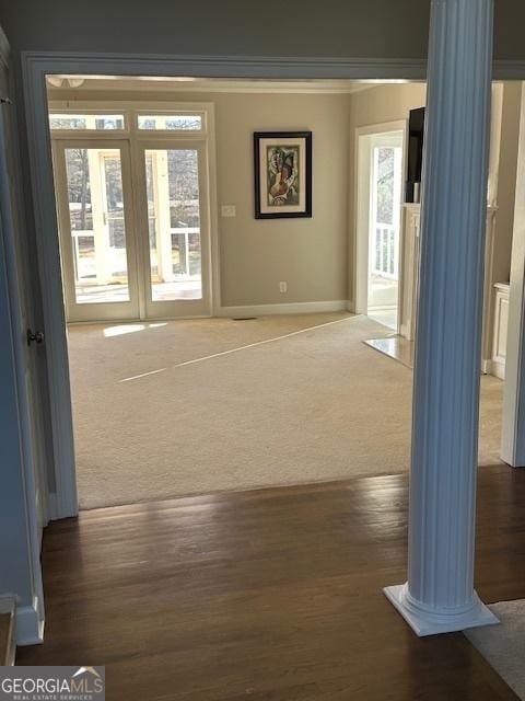 hall featuring ornate columns, crown molding, and dark colored carpet