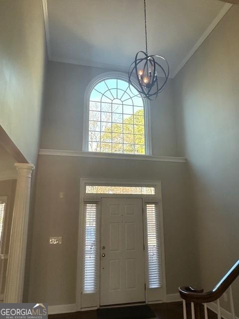 foyer entrance with crown molding, a towering ceiling, and an inviting chandelier