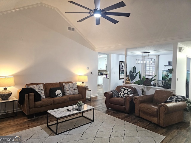 living room with ceiling fan with notable chandelier, dark hardwood / wood-style flooring, crown molding, and vaulted ceiling