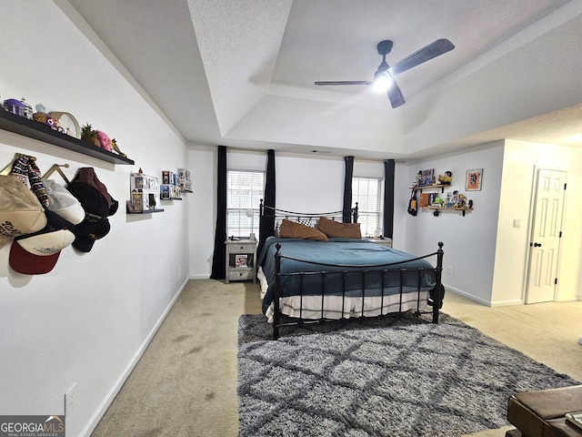 bedroom with ceiling fan, multiple windows, light carpet, and a tray ceiling