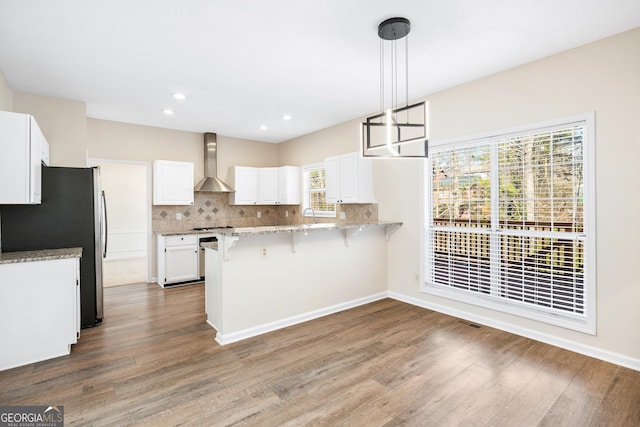 kitchen featuring pendant lighting, wall chimney range hood, white cabinetry, tasteful backsplash, and kitchen peninsula