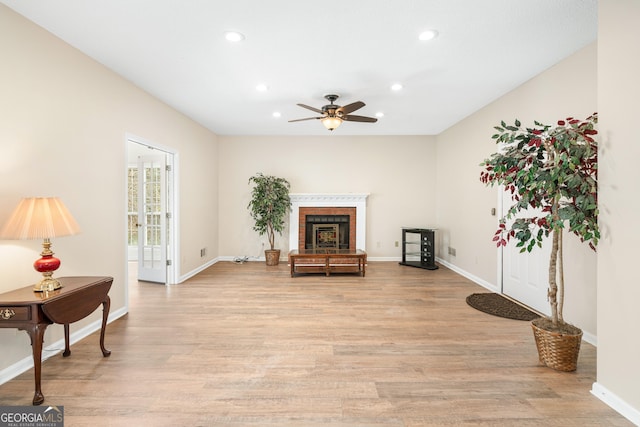 living area featuring ceiling fan, a fireplace, and light hardwood / wood-style floors