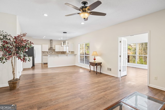 living room with a textured ceiling, ceiling fan, and light hardwood / wood-style flooring