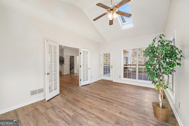 interior space with ceiling fan, hardwood / wood-style floors, a skylight, high vaulted ceiling, and french doors