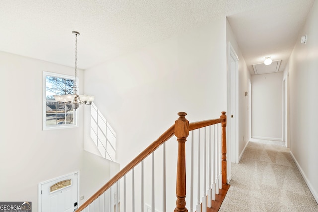 hall featuring light colored carpet, a textured ceiling, and an inviting chandelier