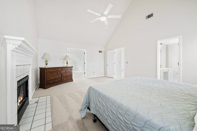 carpeted bedroom with high vaulted ceiling, connected bathroom, a tiled fireplace, and ceiling fan