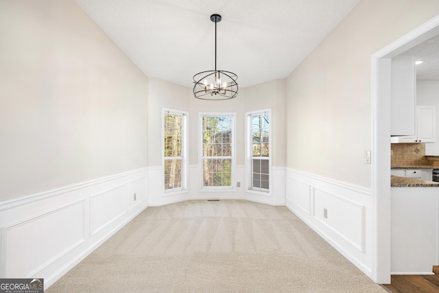 unfurnished dining area featuring light carpet and an inviting chandelier