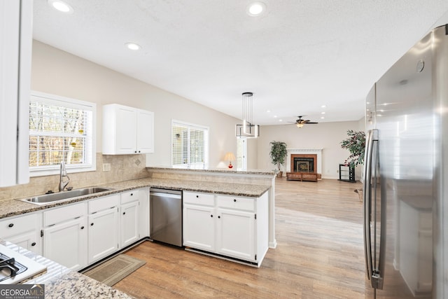 kitchen featuring kitchen peninsula, sink, white cabinetry, hanging light fixtures, and stainless steel appliances