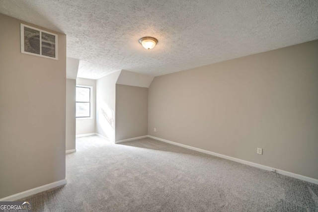 additional living space featuring vaulted ceiling, a textured ceiling, and light colored carpet