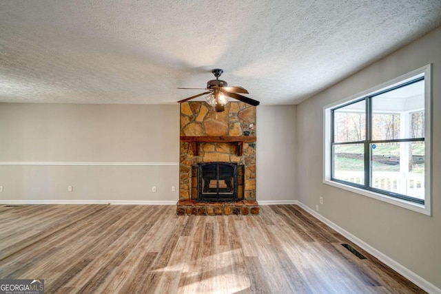 unfurnished living room featuring ceiling fan, wood-type flooring, a stone fireplace, and a textured ceiling