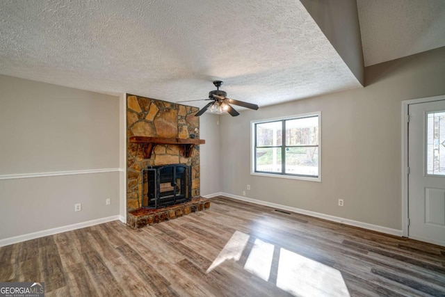 unfurnished living room with ceiling fan, a textured ceiling, hardwood / wood-style flooring, and a fireplace