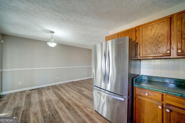 kitchen with tasteful backsplash, stainless steel refrigerator, a textured ceiling, pendant lighting, and light hardwood / wood-style flooring