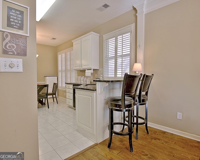 kitchen featuring tasteful backsplash, a wealth of natural light, white cabinets, and dark stone counters