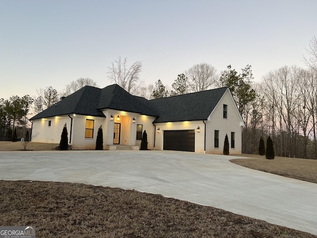 view of front facade featuring a shingled roof, concrete driveway, brick siding, and an attached garage